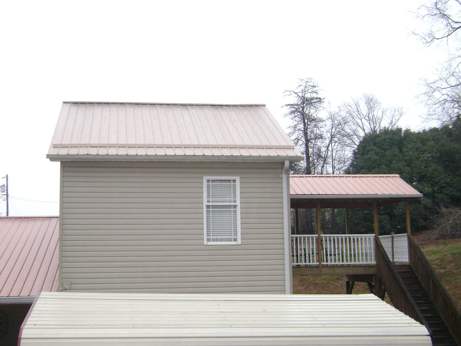 Tan metal roofs on a two story addition and attached porch, from a Roof Replacement job in Warwick